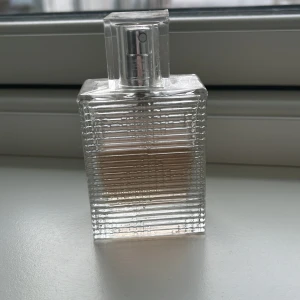  Burbbery parfym - Säljer en elegant parfymflaska med en unik räfflad design. Flaskan är genomskinlig och har en stilren, fyrkantig form med en silverfärgad spraypump. Perfekt för den som gillar en minimalistisk och modern look.