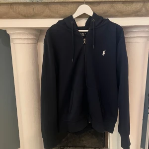Mörkblå  hoodie från Ralph Lauren - Säljer en stilren mörkblå hoodie från Ralph Lauren med dragkedja och det klassiska logotypbroderiet på bröstet. Perfekt för en avslappnad look. Nypris runt 2-2.5k