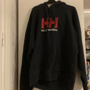 Mörkblå hoodie från Helly Hansen - Säljer en mörkblå hoddie med en ficka på magen. Säljer den då den inte kommer till användning. Få gånger använd så är som ny. Ny pris 700kr