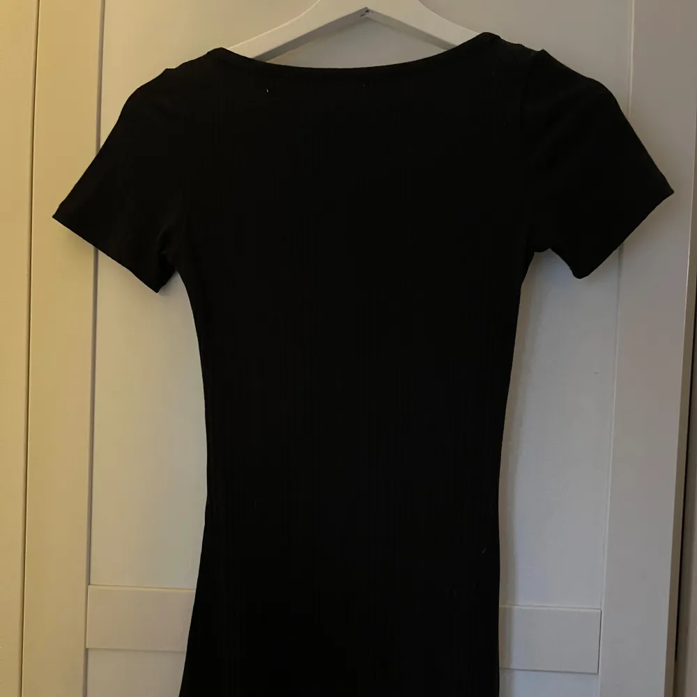 Säljer en svart klänning från Divided med korta ärmar och knappar framtill. Klänningen har en tight passform och är perfekt för en stilren look. Den är tillverkad i ett mjukt material som ger en bekväm känsla.. Mekot.