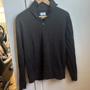Mörkgrå merinoulltröja från These Glory Days - Säljer en stilren mörkgrå tröja i merinoull från These Glory Days. Tröjan har en dragkedja vid halsen och långa ärmar, perfekt för kyligare dagar. Den är både bekväm och elegant, idealisk för lager-på-lager-stil.