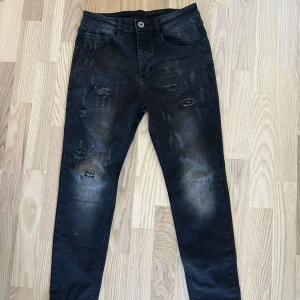Svarta jeans med slitningar - Snygga svarta jeans med slitningar och en knappstängning. De har en klassisk femficksdesign och en modern look med slitna detaljer. Perfekta för en trendig stil.
