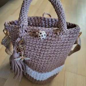 Beige stickad handväska  - Beige stickad handväska med vita ränder och ett prickigt knäppningslock. 🤎Väskan har ett dekorativt hänge med ett glittrigt bi och fransar. Botten är förstärkt med små guld nitar för extra stabilitet.🤎 Väskan är egengjord därav priset.🤎