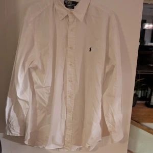 Vit skjorta från Polo Ralph Lauren - Klassisk vit skjorta från Polo Ralph Lauren med broderad logotyp på bröstet. Skjortan har långa ärmar och knappar framtill. Tillverkad i 100% bomull för en bekväm passform. Perfekt för en stilren look. Priset är inte hugget i sten och går att diskuteras 