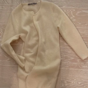 Beige kofta från Tiger of Sweden strl:XS - Säljer en elegant beige kofta från Tiger of Sweden. Den är långärmad och har en stilren design utan knappar. Perfekt för att hålla sig varm och snygg under kyligare dagar.