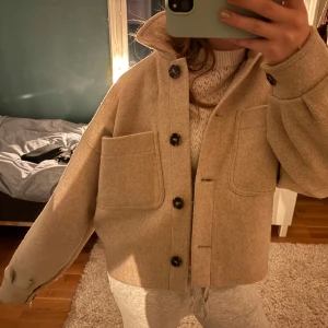 Beige kappa med knappar - Säljer en stilren beige kappa med stora knappar och två framfickor. Jackan har en klassisk design med en bekväm passform och långa ärmar. Perfekt för kyligare dagar.