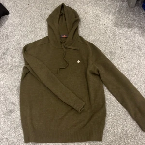 Olivgrön hoodie från Morris - Säljer en stilren olivgrön hoodie från Morris. Tröjan har en liten broderad detalj på bröstet och är tillverkad i ett mjukt material. Perfekt för en avslappnad look.  Det är kasmir