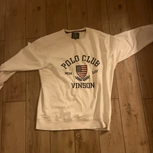 Vit sweatshirt från Vinson Polo Club - Säljer en vit sweatshirt från Vinson Polo Club med tryck på framsidan. Tröjan har långa ärmar och en rund halsringning. Perfekt för en avslappnad stil. Hör av dig vid intresse!