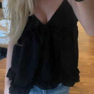 Svart ärmlös topp - Säljer en stilren svart ärmlös topp med volangdetaljer. Perfekt för en avslappnad men chic look. Passar bra till jeans eller kjol.