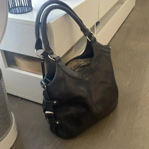 Svart axelväska i skinn - Snygg svart axelväska i äkta läder med dubbla handtag och silverfärgade metalldetaljer. Väskan har en stilren design och är perfekt för att bära med sig det nödvändigaste. Insidan har ett mönstrat foder som ger en extra touch av stil. Så fin i verklighet då den har en speciell färg grå/svart blandning ❤️