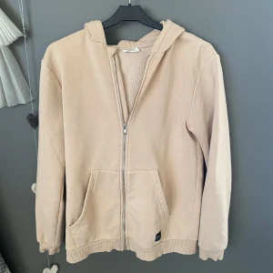 Beige hoodie från Kappahl - Säljer en beige hoodie från Kappahl med dragkedja och fickor framtill. Perfekt för en avslappnad stil. Den har en mjuk insida och en praktisk huva.