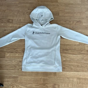Vit hoodie från Peak Performance - Säljer en stilren vit hoodie från Peak Performance. Den har en klassisk design med logotypen tryckt på bröstet och en praktisk huva. Perfekt för en avslappnad look. Hör av dig vid intresse! Är i en S men fittar Xs