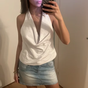Vit halterneck topp - Säljer en stilren vit halterneck topp med draperad framsida och öppen rygg. Perfekt för varma sommardagar eller en kväll ute. Toppen har en elegant och luftig design. aldrig använd, lappen är kvar 🫶
