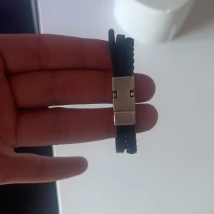 Svart flätat armband med metallspänne - Snyggt svart armband i flätat skinn med ett stilrent metallspänne. Perfekt för att ge en cool touch till din outfit. Passar både till vardag och fest.