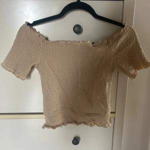 Beige offshoulder topp från H&M - Säljer en beige offshoulder topp från H&M med korta ärmar och en smockad design. Perfekt för en stilren och bekväm look. Toppen har en elastisk passform som ger en snygg siluett. Hör av dig vid intresse! 🌟