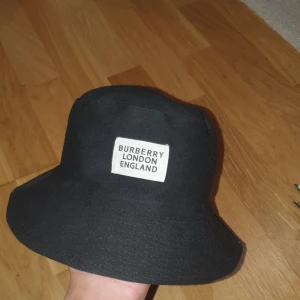 Rutig bucket hat från Burberry - Snygg bucket hat från Burberry med klassiskt rutigt mönster i beige, svart, vit och röd. Perfekt för att ge din outfit en stilren touch.