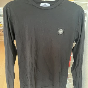 Svart långärmad tröja från Stone Island  - Säljer en stilren svart långärmad tröja från Stone Island . Tröjan har en rund halsringning och ett diskret märke på bröstet. Perfekt för en avslappnad och trendig look.