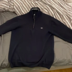 Mörkblå tröja med dragkedja från GANT - Säljer en stilren mörkblå tröja från GANT med dragkedja och hög krage. Tröjan har ett diskret broderat emblem på bröstet och ribbade detaljer vid kragen. Perfekt för en avslappnad men snygg i sociala tillfällen. Inga skador alls, skriv för info och bilder!😇
