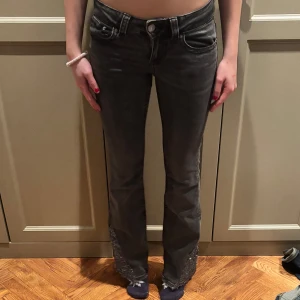 Grå bootcut jeans med paljettdetaljer - Snygga grå bootcut jeans med glittrande paljettdetaljer på bakfickorna. Perfekta för att ge en extra touch till din outfit. Jeansen har en klassisk design med en modern twist.
