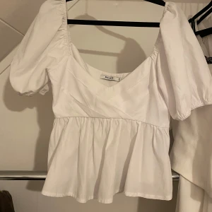 Vit blus från NA-KD - Säljer en söt vit blus från NA-KD med puffiga kortärmar och v-ringning. Blusen har en volangdetalj i nederkant. Perfekt för sommarens alla tillfällen🩷