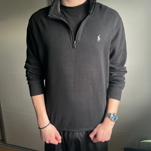 Svart tröja med dragkedja från Polo Ralph Lauren - Säljer en stilren svart tröja från Polo Ralph Lauren med halv dragkedja och det ikoniska logotypbroderiet på bröstet. Perfekt för en avslappnad men ändå elegant look. Tröjan är använd några gånger men skicket är bra 9/10. Nypris 2200kr mitt 399kr.