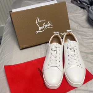 Vita sneakers från Christian Louboutin - Snygga vita sneakers från Christian Louboutin med den ikoniska röda sulan. Skorna har en klassisk design med snörning och rund tå. Perfekta för att ge din outfit en lyxig touch.