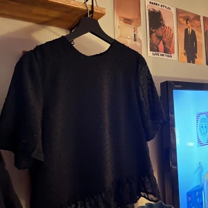 Svart blus från NA-KD - Snygg svart blus från NA-KD med diskreta prickar och volangdetalj vid nederkanten. Perfekt för en stilren look💗