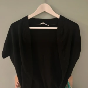 Svart bolerotopp - Säljer en stilren svart bolerotopp med korta ärmar. Perfekt för att lägga till en extra touch till din outfit. Passar bra över klänningar eller toppar.