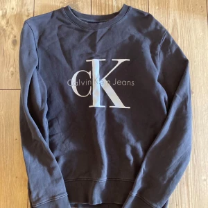 Mörkblå tröja från Calvin Klein Jeans - Säljer en snygg mörkblå tröja från Calvin Klein Jeans med deras ikoniska logga på framsidan. Tröjan har långa ärmar och en rund halsringning. Perfekt för en stilren och avslappnad look. Vid frågor är det bara att skicka🌟