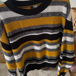 Randig stickad tröja - Säljer en snygg randig stickad tröja i svart, vit och gul. Tröjan har långa ärmar och en rund halsringning. Perfekt för att hålla sig varm och stilren under kyligare dagar.