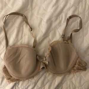Beige bh med spetsdetaljer från Chantelle - Elegant beige/puderrosa bh från Chantelle med spetsdetaljer och en söt rosett framtill. Justerbara axelband och hakknäppning bak. Uppskattningsvis strl 70B. 