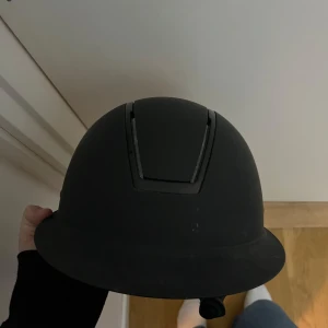 Svart ridhjälm - Säljer en stilren svart ridhjälm med en slät yta och justerbart hakband. Perfekt för ridning och säkerhet. Hjälmen har en diskret design och är bekväm att bära. Har andvänt i ca 1 år inga sprickor eller något sådant. Storlek ca M/L Nypris var 1500 kr säljer nu för 600 kr pris kan diskuteras! 