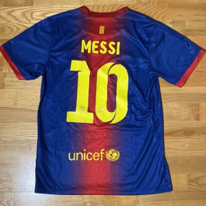 Blå och röd fotbollströja från Nike - Säljer en blå och röd fotbollströja från Nike med korta ärmar. Tröjan har ett tryck med 'Qatar Foundation' och klubbmärke på framsidan samt 'Messi 10' på baksidan. Perfekt för fotbollsfans! 💙❤️