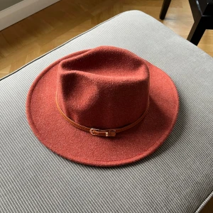 Rostfärgad hatt i ullblandning  - Snygg rostfärgad hatt med ett bälte runt kullen. Innermått 58 cm
