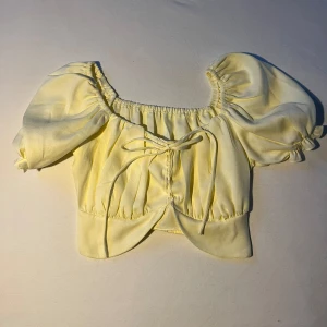 Gul blus med puffärmar - Säljer en söt gul blus med puffiga kortärmar och knytning framtill. Perfekt för sommaren och är i nyskick. 