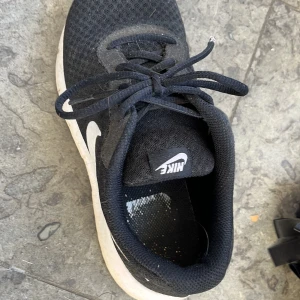 Svarta Nike sneakers - Säljer ett par svarta Nike sneakers med vit sula och klassisk snörning. Perfekta för vardagsbruk och träning. De har en rund tå och är gjorda i syntetmaterial för extra komfort.