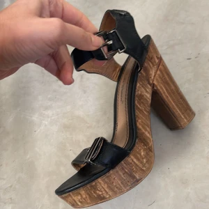 Svarta sandaler med träklack - Snygga svarta sandaler med bred träklack och justerbara spännen. Perfekta för att ge lite höjd och stil till din outfit. Sandalerna har en öppen tå och en robust design som kombinerar både komfort och mode.