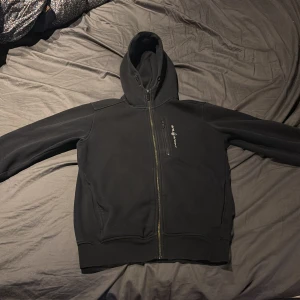 Svart Sail Racing hoodie - Säljer en svart hoodie med dragkedja och huva.