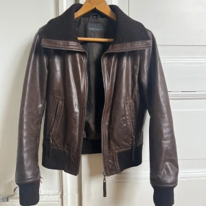 Brun skinnjacka med dragkedja - Snygg brun skinnjacka från Rock’n Blur med dragkedja och ribbade detaljer vid krage, ärmslut och nederkant. Jackan har en klassisk bomberstil med två framfickor med dragkedja samt en innerficka. Storlek M men liten i storelk, skulle snarare säga en tight S! Lite slitningar men det tillhör looken. Skriv om du har frågor❤️