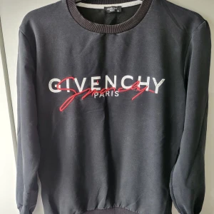 Svart tröja från Givenchy - Säljer en stilren svart tröja från Givenchy med deras ikoniska logga i vitt och rött på framsidan. Tröjan har långa ärmar och ribbade muddar vid ärmslut och nederkant. Perfekt för en casual look. Äkta 
