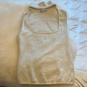 Beige ribbad ärmlös topp från Zara - Säljer en beige ribbad ärmlös topp från Zara med hög krage och fyrkantig urringning. Toppen har en mjuk och stretchig känsla, perfekt att styla med jeans eller kjol. Enkel men trendig design som passar till många olika looks.