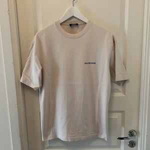 Beige t-shirt från Balenciaga XS - Beige t-shirt från Balenciaga i unisexmodell. T-shirten har blå Balenciaga-tryck fram och bak. Size xs men passar s-m då den är oversize. Köpt på Farfetch.