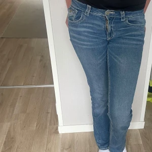 Blå bootcut jeans från Gina Tricot - Snygga blå bootcut jeans från Gina Tricot med klassisk femficksdesign och dekorativa sömmar på bakfickorna. Jeansen har låg midja och är tillverkade i mjukt denimtyg med lätt slitning för en cool look. En lagning precis vid högra bakfickan men man ser inte sömmen när jeansen är på