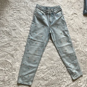 Baggy ljusblå jeans med broderade blommor - Säljer ett par baggy ljusblå jeans från H&M med justerbar midja. Jeansen har broderade små blommor över hela byxorna och klassisk femficksmodell. Perfekta för dig som gillar en avslappnad och trendig stil.