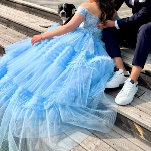 Ljusblå prinsessklänning med spets - Magisk ljusblå långklänning med voluminös tyllkjol och offshoulder-ärm. Klänningen är beställd från Cargo Clothing i Storbritannien. Klänning är från kollektionen By Cinderella Divine. Köptes för 2300kr plus 500kr tull (sammanlagt 2800kr). Klänningen är endast använd 1 gång utan några defekter. Står UK10 som storlek vilket enligt deras hemsida motsvarar EU 42 vilket ej stämmer då jag är en storlek 36 för referens och är 164cm lång. Inga ändringar på klänningen har gjorts. Kontakta mig för frågor