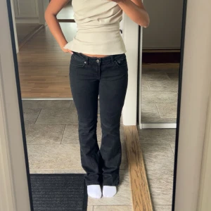 Svarta bootcut jeans - Säljer ett par svarta jeans med bootcut-modell och låg midja. Jeansen har klassisk femficksdesign och är i ett stretchigt denimtyg som sitter snyggt över höfterna och låren. Perfekta för dig som gillar en tidlös och clean look.