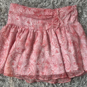 Rosa och vit kortkjol med paisleymönster - Supersöt kortkjol i rosa och vitt med paisleyinspirerat mönster. Kjolen har en bred linning och är lätt utställd med volangig känsla. STL 158/168!!!!