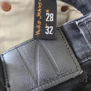 Svarta jeans från Nudie Jeans, 28/32 - Snygga svarta jeans från Nudie Jeans med klassisk femficksdesign och diskret logga på bakfickan. Jeansen har en mörk tvätt och raka ben, tillverkade i mjuk bomullsdenim. Perfekta för en clean och stilren look.