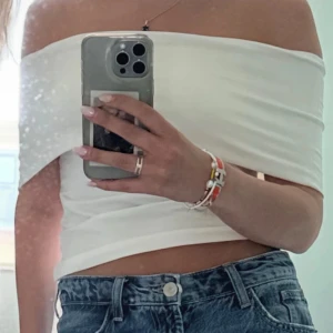 Vit offshoulder topp  - Säljer en stilren vit offshoulder topp med croppad passform. Toppen är ärmlös och har en bred kant som vilar snyggt över axlarna. Perfekt att matcha med jeans eller kjol för en clean look. Liten fläck fram se sista bilden.
