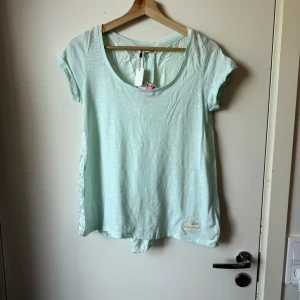Mintgrön t-shirt från Odd Molly - Superfräsch mintgrön t-shirt med rund halsringning och korta ärmar. T-shirten är i mjuk bomull och har en relaxed passform. Perfekt för dig som gillar en enkel men snygg look. Liten Odd Molly-label nertill. Från märket Odd Molly i storlek 0 som enligt deras storleksguide motsvarar ungefär en Storlek XS. Helt ny med tags. Men se sista bild för defekt, 